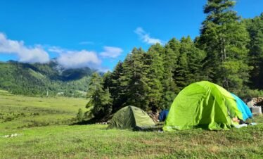 Explore serene camping with green tents amidst Bhutan's lush landscapes under a vibrant blue sky.