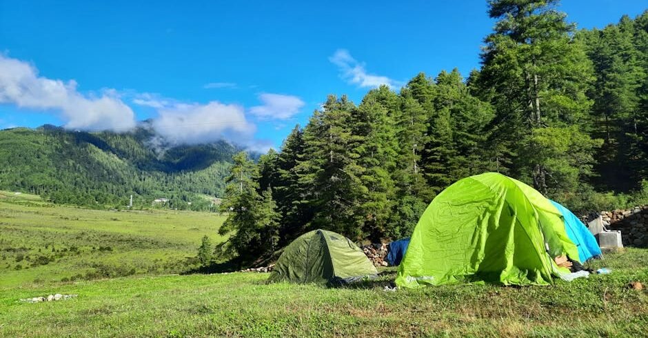 Explore serene camping with green tents amidst Bhutan's lush landscapes under a vibrant blue sky.