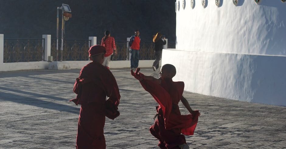 Two young monks captured outdoors in traditional attire, playfully engaging at a temple site.