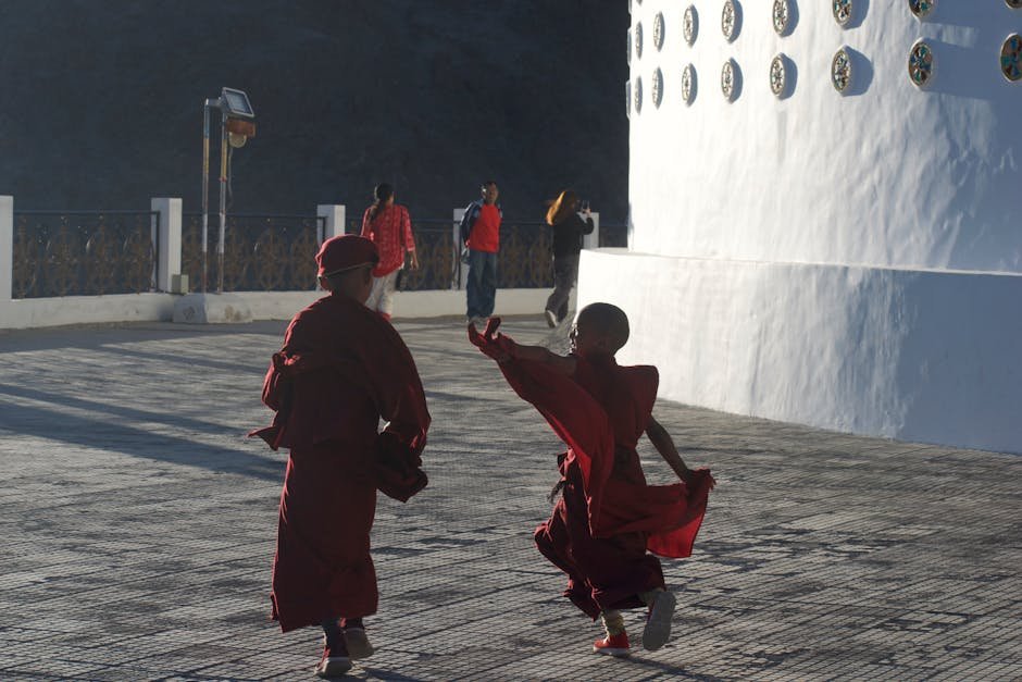 Two young monks captured outdoors in traditional attire, playfully engaging at a temple site.